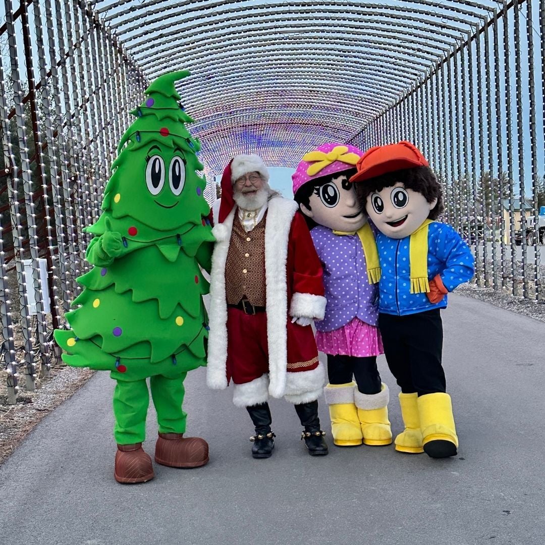 An image of Santa, Sofia, Jax, and Evy the Evergreen posing for a picture under the Light Tunnel. An image of Santa, Sofia, Jax, and Evy the Evergreen posing for a picture under the Light Tunnel.