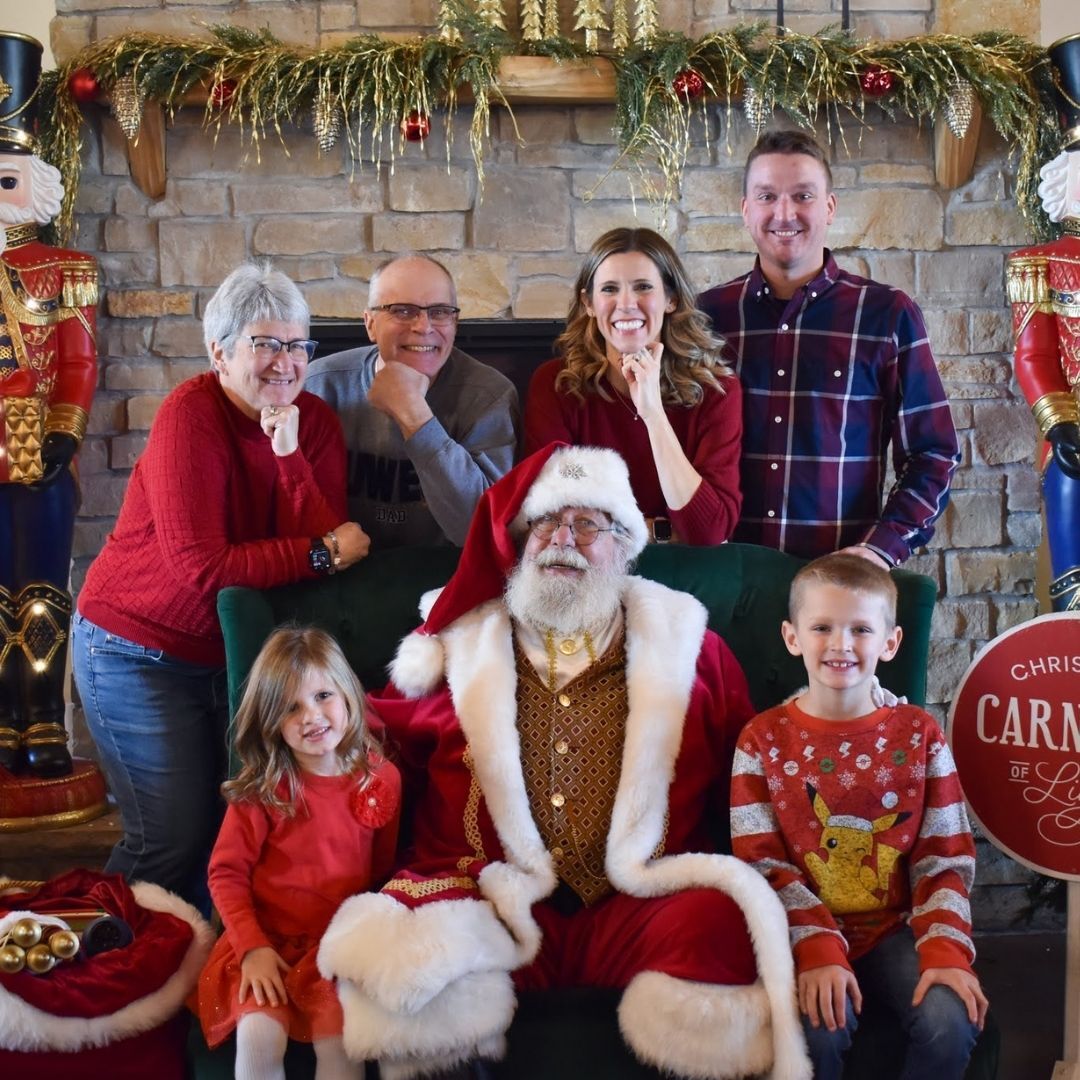 An image of a large family posing for a picture with Santa at his workshop.